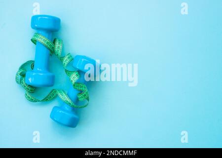 Kurzhanteln, Turnschuhe, Maßband, Wasserflasche und Notizblock auf blau. Stockfoto