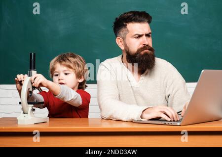 Vater und Sohn. Vorschulschüler. Der Lehrer bringt einem Schüler die Verwendung eines Mikroskops bei. Glückliche Familie - Daddy und Sohn zusammen. Grundschüler und Stockfoto