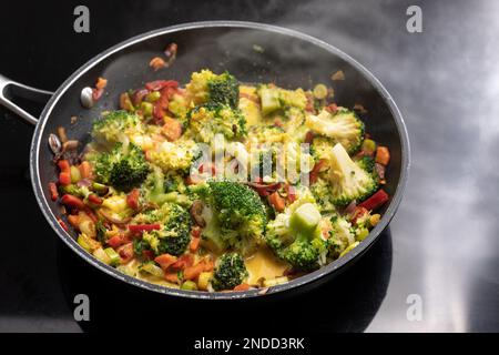 Vegetarisches Curry mit Brokkoli und anderem Gemüse in einer dampfenden Bratpfanne auf einer schwarzen Herdplatte, asiatisches Kochkonzept, Kopierbereich, ausgewählter Fokus, n Stockfoto