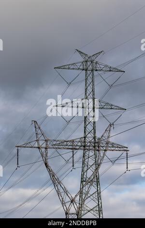 Die Silhouette eines Hochspannungspylons vor einem dramatisch bewölkten Himmel. Entwicklung von Hochspannungsübertragungsnetzen Stockfoto