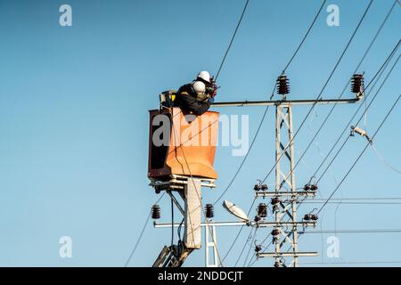 Elektroarbeiter stellen eine Hochspannungsverbindung her. Strommasten und -Kabel. Stockfoto