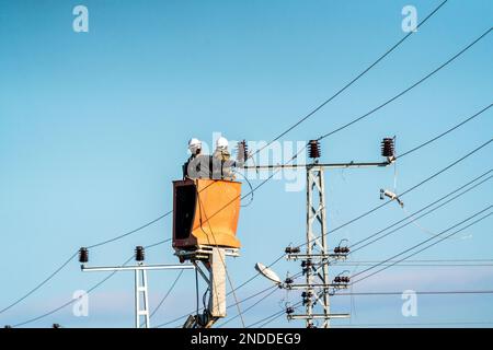 Elektroarbeiter stellen eine Hochspannungsverbindung her. Strommasten und -Kabel. Stockfoto