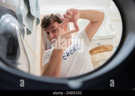 Männeransicht von der Waschmaschine drinnen. Männchen macht täglich Wäsche. Ich habe einen Bilderrahmen mit den Fingern gemacht. Stockfoto