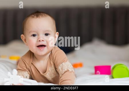 Baby bis zu einem Jahr, liegt auf dem Bett zwischen Spielzeug Stockfoto