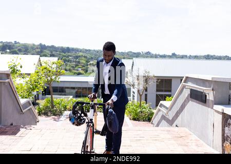 Ein afroamerikanischer Geschäftsmann, der Anzug trägt und mit dem Fahrrad zur Arbeit geht, mit einer Tasche Stockfoto