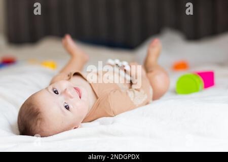 Baby bis zu einem Jahr, liegt auf dem Bett zwischen Spielzeug Stockfoto