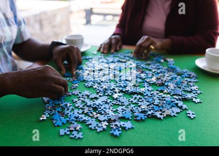 Mittelteil eines afroamerikanischen Seniorenpaares, das zu Hause Puzzle löst. Altersruhestandsleben und Lebenskonzept Stockfoto