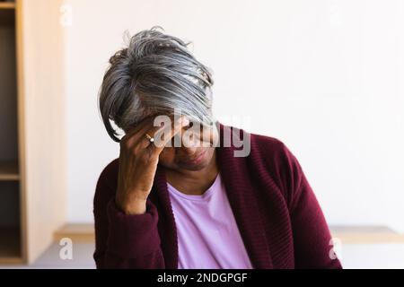 Gestresste afroamerikanische Seniorin, die ihren Kopf zu Hause hält. Altersruhestandsleben und Lebenskonzept Stockfoto