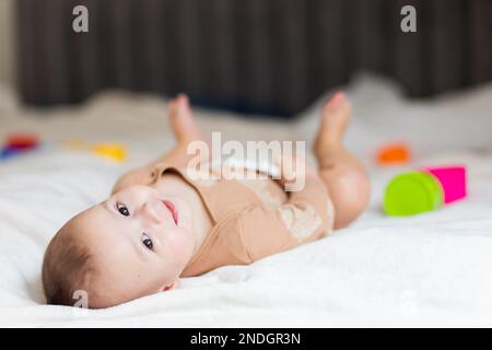 Baby bis zu einem Jahr, liegt auf dem Bett zwischen Spielzeug Stockfoto