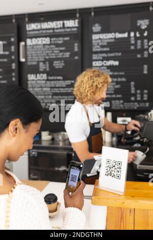 Glücklicher, vielseitiger Barista und eine Frau, die qr-Code mit einem Smartphone im Café scannt. Café, Freizeit und Stadtkonzept. Stockfoto