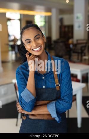 Porträt einer fröhlichen, birassischen Barista, die eine Schürze im Café trägt. Café, Freizeit und Stadtkonzept. Stockfoto