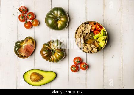 Ein Stillleben mit Salat mit verschiedenen Arten gewürfelter Tomaten, Avocado und viel Thunfisch in Dosen, süßen Marmeladentomaten, einer halben Avocado mit Samen und Stockfoto