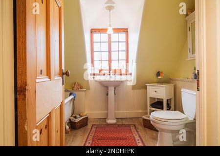 Freistehende Badewanne mit Rollbett, Standwaschbecken und Toilette im oberen Badezimmer mit ausgeblichenen Pinienholzböden im alten renovierten Haus aus den 1650er Jahren. Stockfoto