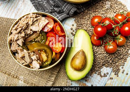 Ein wunderbarer Thunfischkonserven-Salat mit gewürfelten Tomaten und Avocados in einer goldenen Schüssel mit Pepita-Tomaten und Avocado über getrockneten Linsen Stockfoto