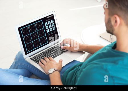 Ein Mann spielt Sudoku-Spiel auf einem Laptop drinnen, Nahaufnahme Stockfoto