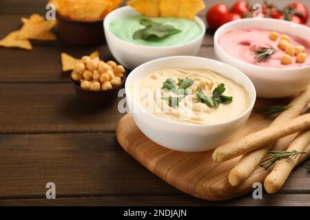 Verschiedene Arten von leckerem Hummus serviert mit Brotstangen auf einem Holztisch Stockfoto