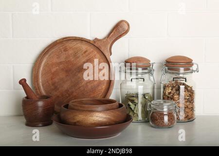 Geschirr aus Holz und verschiedene Produkte auf grauem Tisch in der Nähe von weißen Backsteinwänden in der Küche Stockfoto