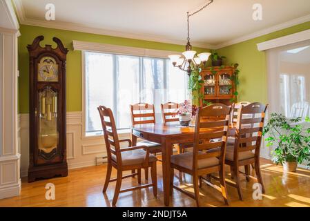 Großväteruhr, Eschenholztisch und Stühle sowie Buffet im Speisesaal mit Eichenholzdielen im Landhaus. Stockfoto