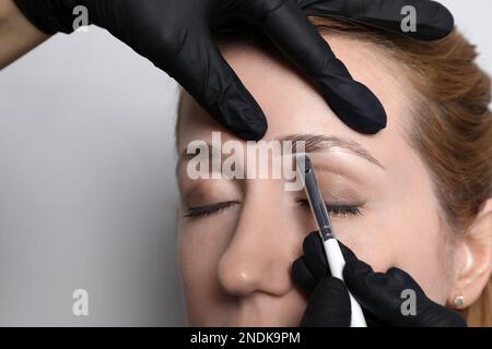 Kosmetikerin, die bei Augenbrauenkorrekturverfahren Farbtöne auf hellgrauem Hintergrund aufträgt, Nahaufnahme Stockfoto