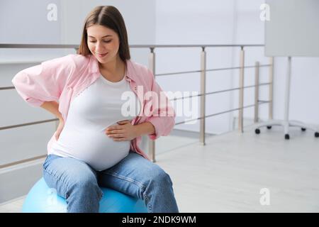 Schwangere Frau, die drinnen auf einem Fitnessball sitzt. Platz für Text Stockfoto