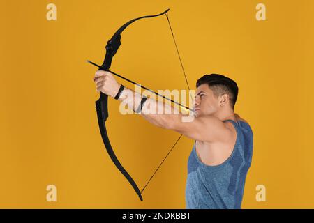 Mann mit Pfeil und Bogen, der Bogenschießen auf gelbem Hintergrund praktiziert Stockfoto