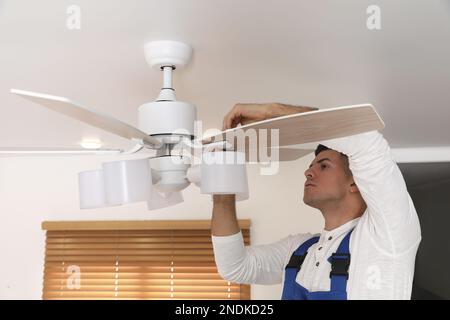 Elektriker repariert Deckenventilator mit Lampen im Innenbereich Stockfoto