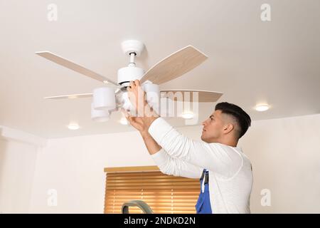 Elektriker repariert Deckenventilator mit Lampen im Innenbereich Stockfoto