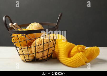 Weiches gelbes Wollgarn mit Stricknadeln und Pullover auf weißem Tisch Stockfoto