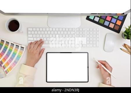 Moderne Grafikdesignerin mit Blick auf den Schreibtisch, Eine Grafikdesignerin, die an ihrem Schreibtisch arbeitet und Tablet und Computer verwendet. Tablet-Modell mit weißem Bildschirm Stockfoto