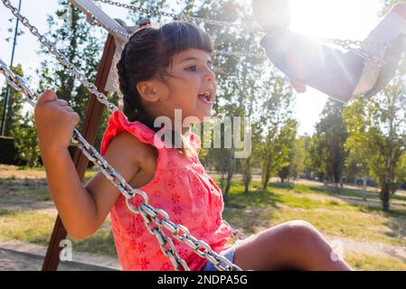 Zwei Kinder, die Spaß haben, zusammen mit der Schaukel auf einem Spielplatz in einem Park zu spielen. Stockfoto