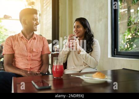 Glückliches, vielfältiges Paar, das fruchtige Drinks genießt und sich beim Treffen im Café unterhalten kann Stockfoto