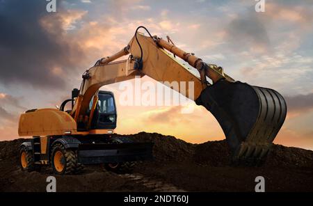 Radbagger bei der Arbeit, der bei Sonnenuntergang Erde gräbt. Stockfoto