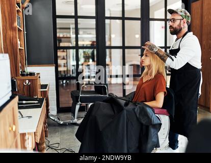 Wie kurz soll es diesmal sein? Eine lange Aufnahme einer attraktiven jungen Frau, die ihr Haar stylen und von einem Friseur behandelt wird Stockfoto