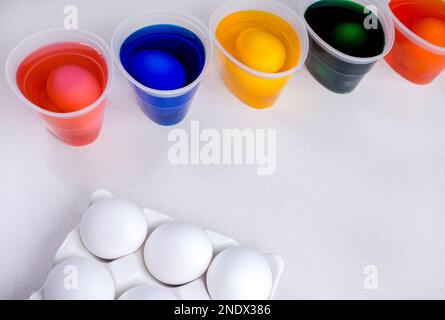 Werkzeuge zum Malen von ostereiern, Eierschachtel, Tassen mit bunten Farben, ostereier, Teller, Pinsel und Farben auf der Seitenansicht des Tisches. Stockfoto