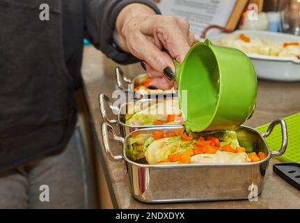 Der Koch gießt Sauce auf Kohlbrötchen mit Lachs und Karotten in der Küche. Französisches Rezept. Stockfoto