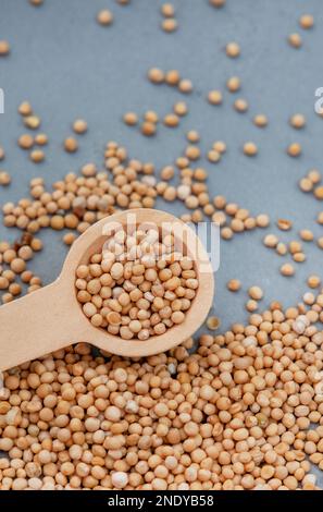 Gelbe Senfkörner mit Löffel auf melierter grauer Oberfläche Stockfoto