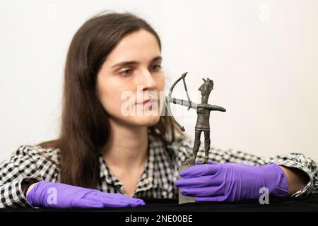 Olivia Maguire inspiziert eine Bronzefigur eines Bogenschützen (1000???700 BCE), die im Heiligtum Abini Teti auf Sardinien ausgegraben wurde, wie sie im Fitzwilliam Museum der Universität Cambridge vor der Ausstellung „Islanders: The Making of the Mediterranean“ installiert ist. Vom 24. Februar bis zum 4. Juni zeigt die Ausstellung Sardiniens berühmte Votivfiguren aus Nuragischer Bronze (bronzetti), die erstmals vom Archäologischen Nationalmuseum von Cagliari in Sardinien (Italien) an das Vereinigte Königreich ausgeliehen werden. Bilddatum: Mittwoch, 15. Februar 2023. Stockfoto