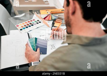 Er denkt an das Design. Ein nicht wiedererkennbarer männlicher Architekt, der mit einigen Bauplänen in einem modernen Büro arbeitet. Stockfoto