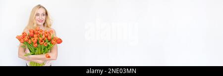 Internationaler Frauentag. Äußerst glückliche Frau mit Blumenstrauß, die rote Tulpen in den Händen hält, auf einem hellen Hintergrund Stockfoto