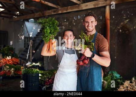 Alles wächst mit Liebe auf dieser Farm. Portrait eines glücklichen jungen Paares, das zusammen posiert und frisch gepflückte Karotten und Rote Bete hält Stockfoto