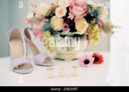 Eheringe liegen auf Süßigkeiten auf dem Tisch neben dem Blumenstrauß und den Brautschuhen Stockfoto