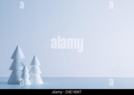 Kleine keramische Weihnachtsbäume auf weißem Hintergrund in kaltem, weichem Winterlicht Stockfoto
