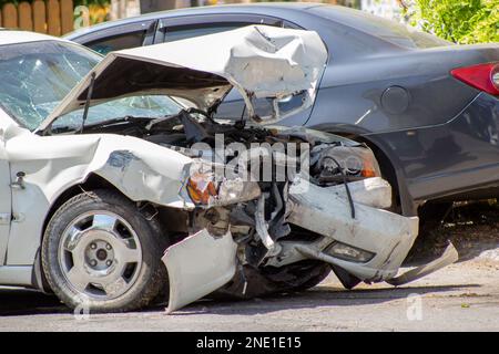 Zwei Autos auf der Straße nach einer Kollision. Abenteuer auf der Straße und kaputte Stoßfänger, Motorhaube, Scheinwerfer und Kotflügel in einem weißen Auto Stockfoto