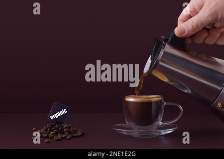 Man gießt frischen heißen Kaffee von Hand aus einer Mokka-Tasse in eine Glastasse. Hintergrund mit Kopierbereich. Stockfoto