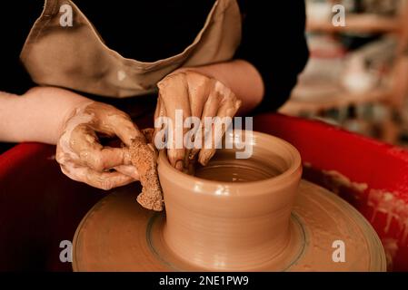 Töpferei kann ein chaotisches Geschäft sein. Eine unerkennbare Frau, die Ton auf einem Töpferrad formt. Stockfoto