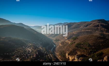 Luftaufnahme einer kleinen ländlichen Stadt, eingebettet zwischen Hügeln, am Rand einer Klippe mit entfernten Bergketten im Hintergrund Stockfoto