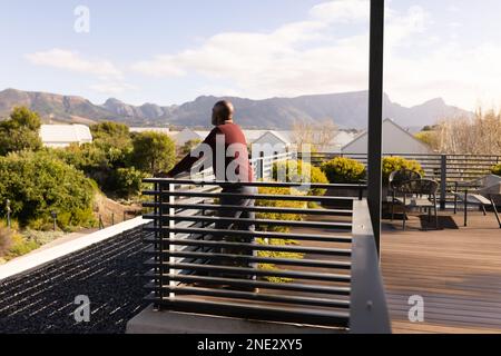 afroamerikanischer Seniorenmann, der die Aussicht genießt, während er zu Hause auf der Terrasse steht. Altersruhestandsleben und Lebenskonzept Stockfoto