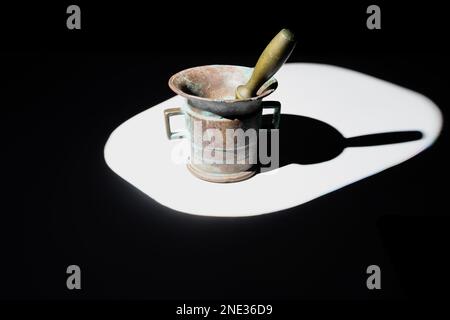 Bronzemörtel und Stößel mit Patina bedeckt, beleuchtet durch einen harten Lichtstrahl. Stockfoto