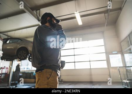 Ein kleiner Winkel von einem Mechaniker, der in einer Werkstatt telefoniert. Hochwertiges Foto Stockfoto