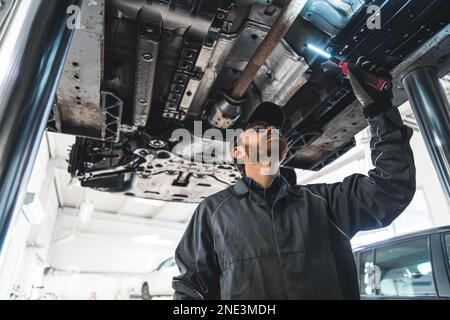 Ein kleiner Winkel von einem Mechaniker, der das Fahrgestell inspiziert und eine Taschenlampe in der Hand hält. Hochwertiges Foto Stockfoto